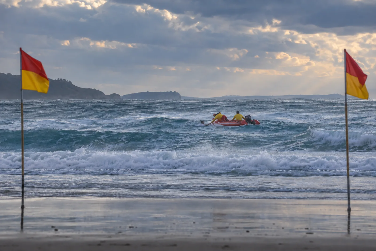 Two lifesavers in an inflatable rescue boat pulling a swimmer from rough surf, between the red and yellow flags.