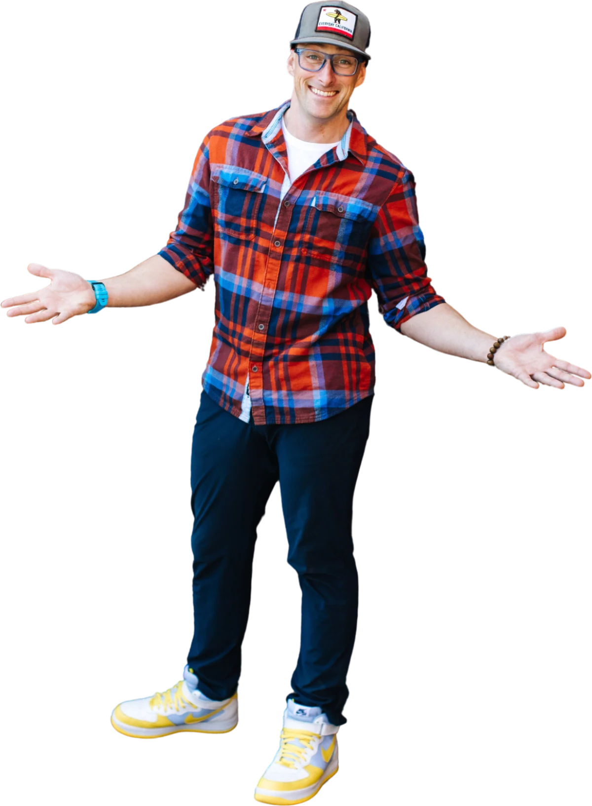 Steve Corney standing with his arms open, in a plaid shirt, cap and sneakers.